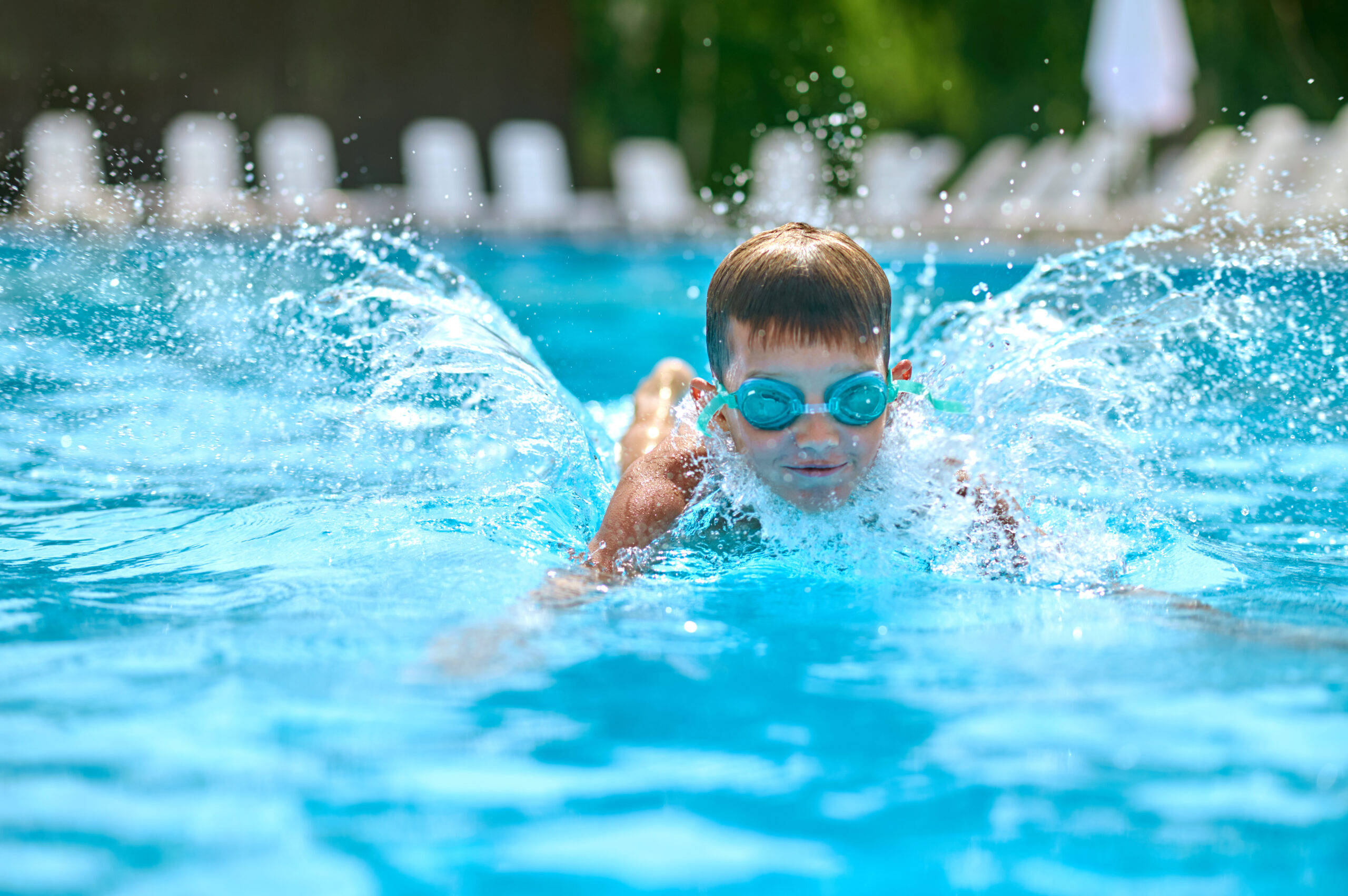 Boy in goggles swimming splashing in pool Pleasure, swimming. Boy in swimming goggles vigorously swimming splashing in pool outdoors on fine day